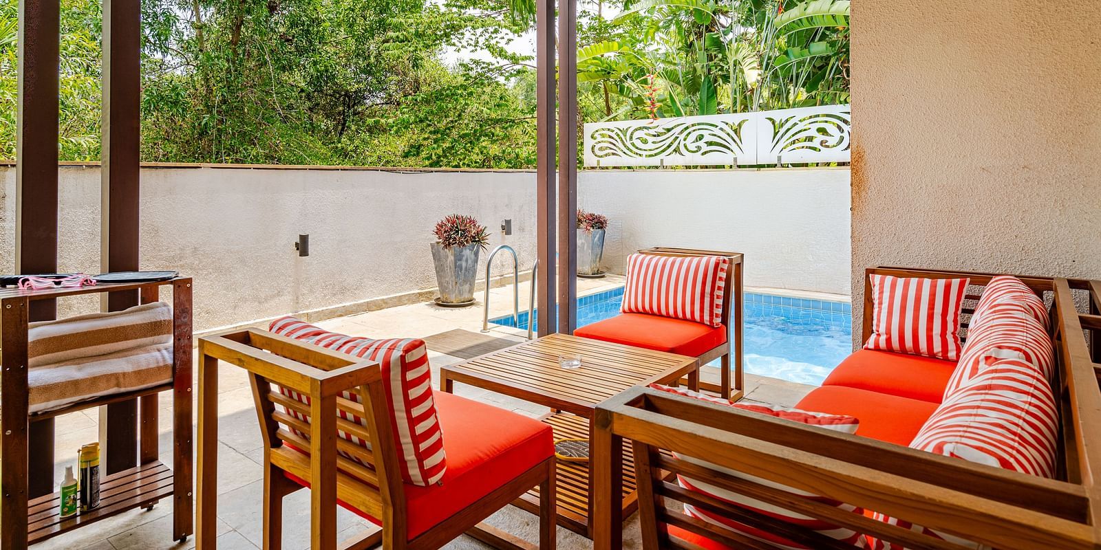Cosy outdoor patio with red and white striped cushioned wooden furniture, a small private pool, tropical plants in the background, and a shaded wooden ceiling providing a relaxing ambience - Lindsay Manor