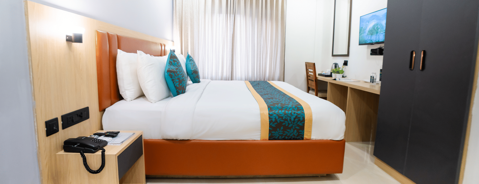 A room with a bed, cabinets, a wall-mounted television, and a side table at Sunrise Business Hotel, Hyderabad.