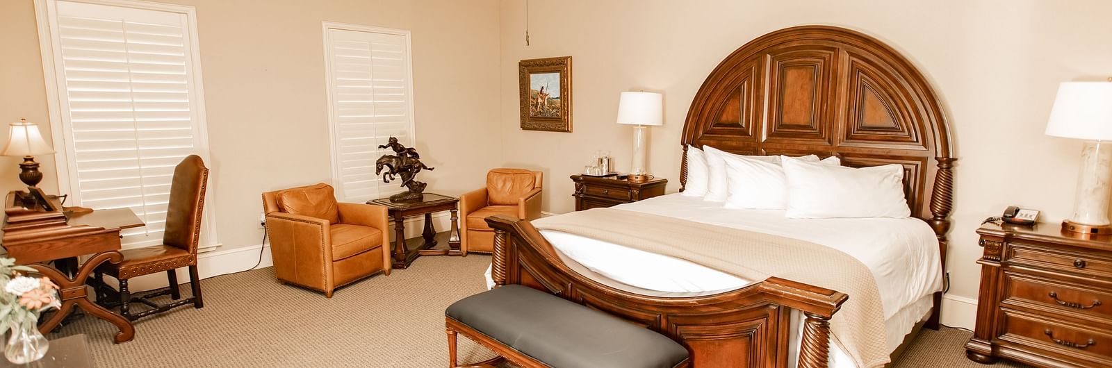 Bedroom with wooden bed and leather seating at The Grand Hotel & Ballroom, McKinney.
