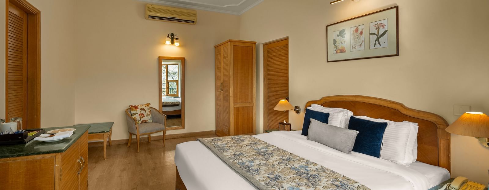 A side view of Superior Cottage Hill View bedroom showcasing a double bed, a side table, and a wardrobe with a mirror adjacent to it -  Baikunth resort, kasauli 