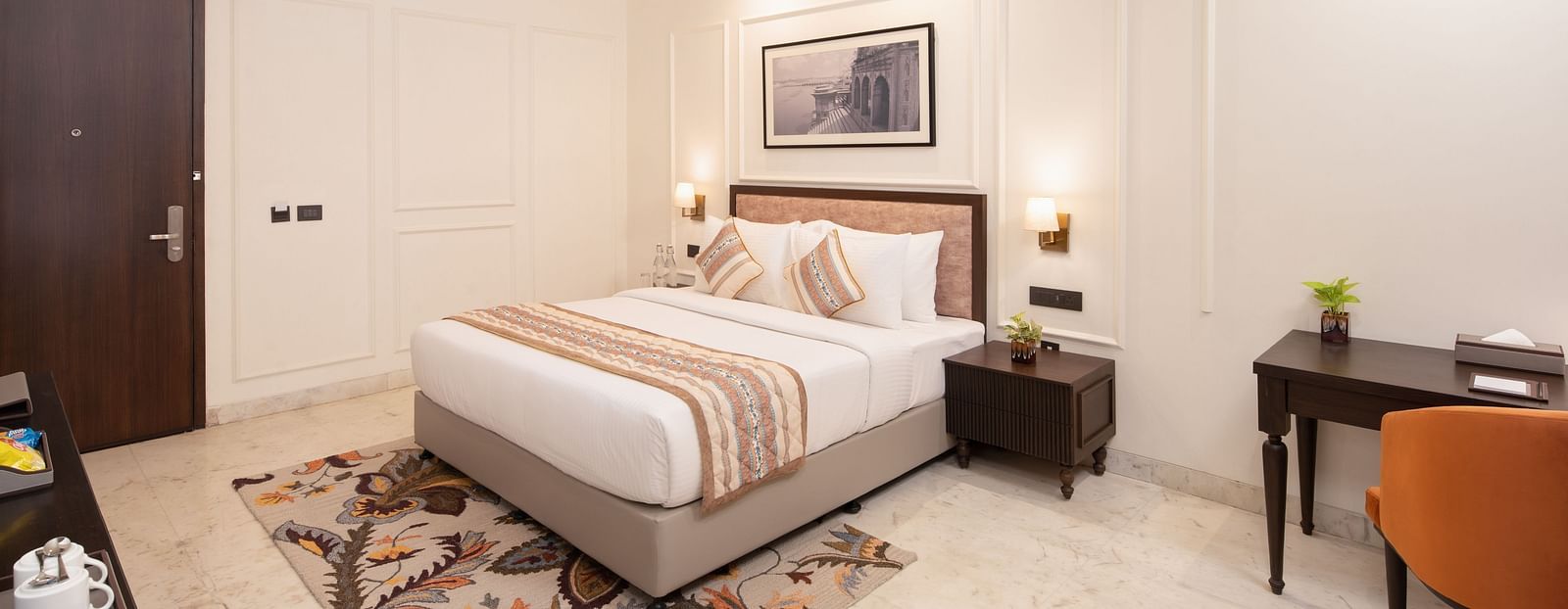 An image of a bedroom with bedside table, photo frame hanged on the wall, work desk with sofa chair, and a flat TV screen - Brij Eternity, Vrindavan