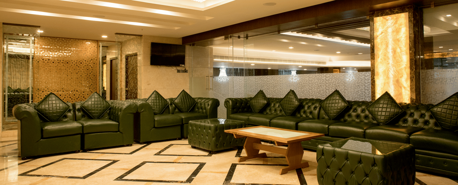 A spacious lounge area at Benzz Park Chennai with dark green sofas and a patterned floor, ideal for relaxation.