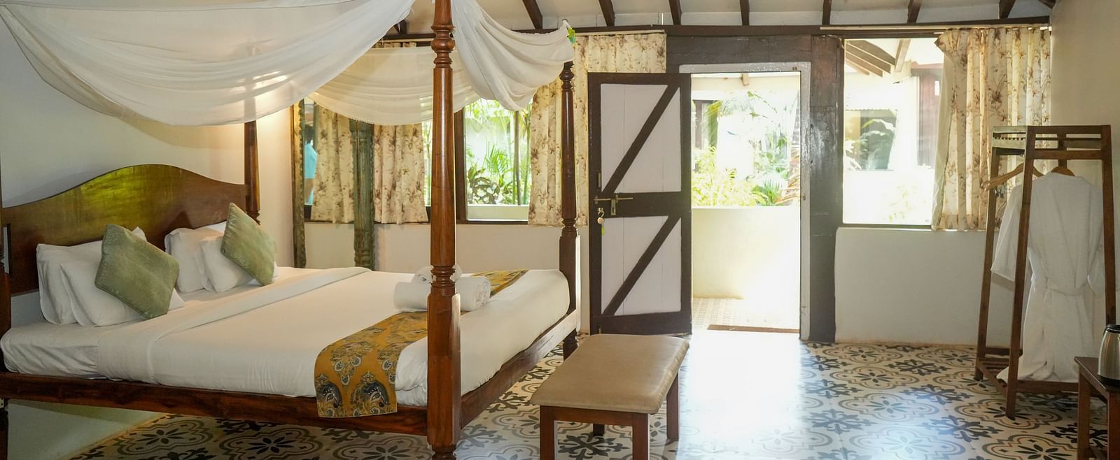 Side view of a spacious room with a large bed, wooden interiors, and a doorway leading outside at De Soul Santé, Morjim.