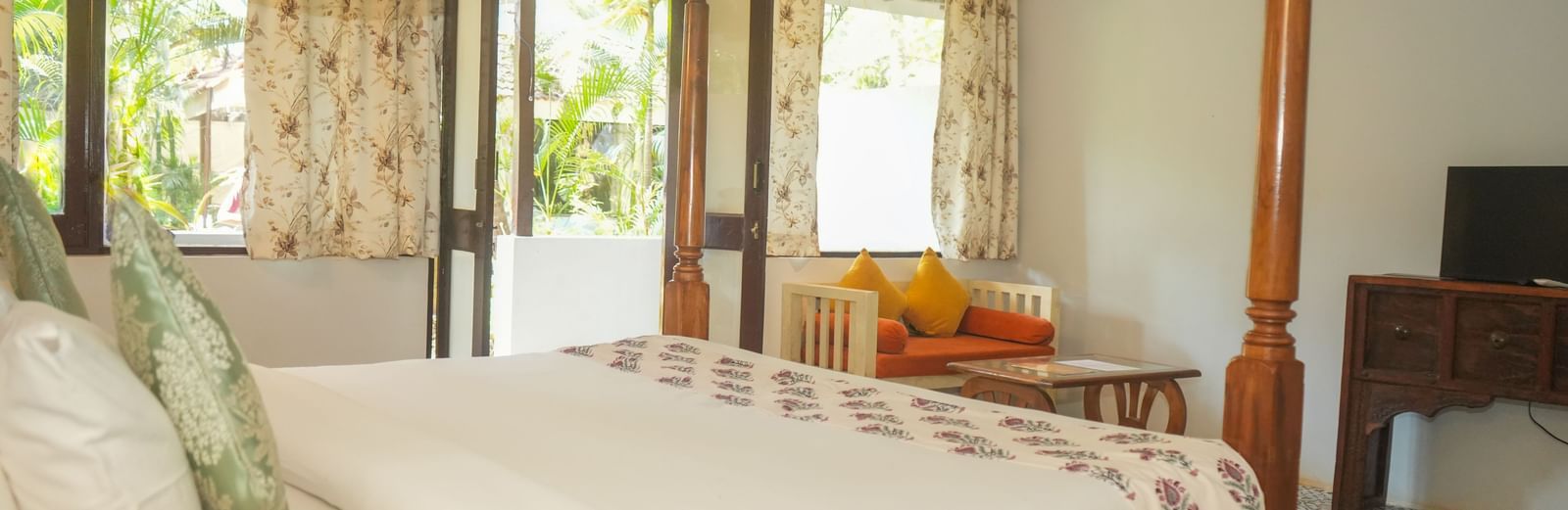 Side view of a canopy bed near large windows overlooking greenery at De Soul Santé, Morjim.