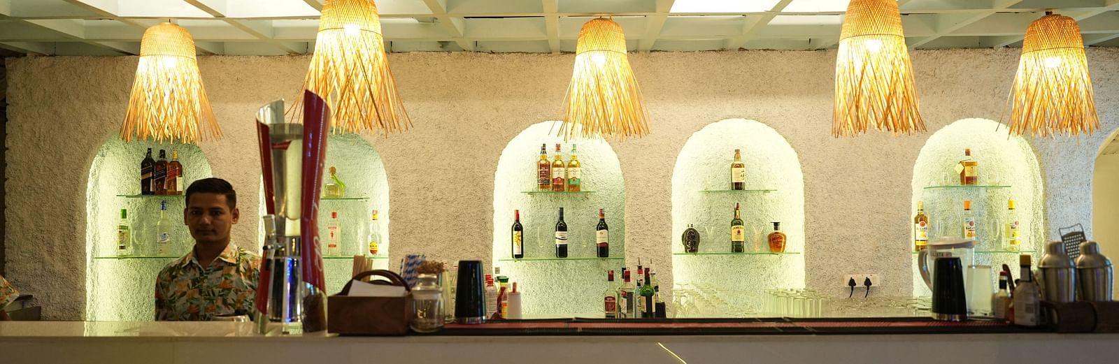 A bar counter in a restaurant at Paradise Isle Beach Resort, Udupi with decorative lights hanging over it