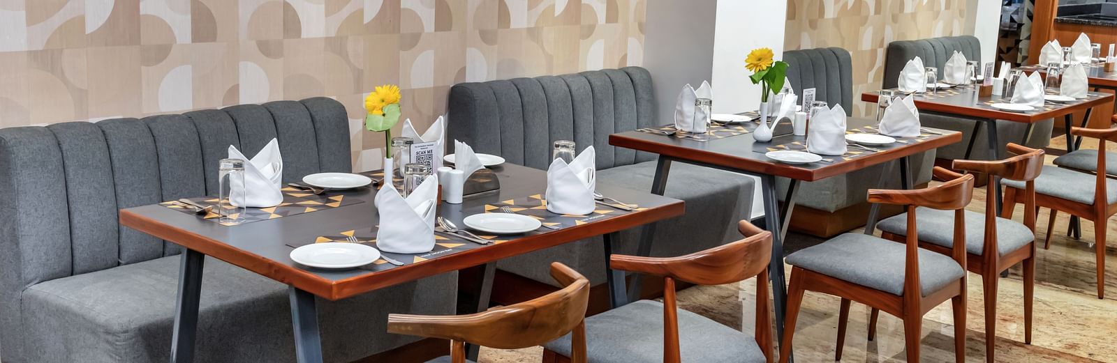 A well-lit restaurant dining area with multiple tables set with plates, cutlery, napkins, and flowers, along with comfortable seating against a patterned wall  | The Citi Residenci Hotel Banskopa