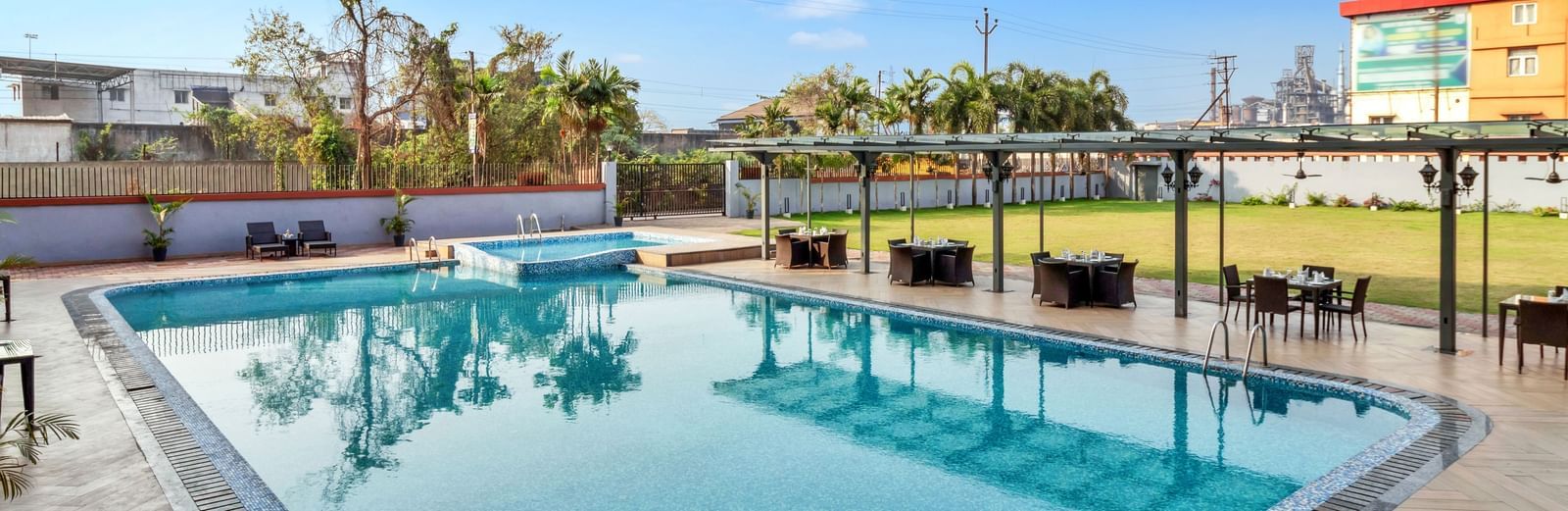 A large outdoor swimming pool with clear blue water, surrounded by lounge chairs and covered seating areas on a sunny day | The Citi Residenci Hotel Banskopa