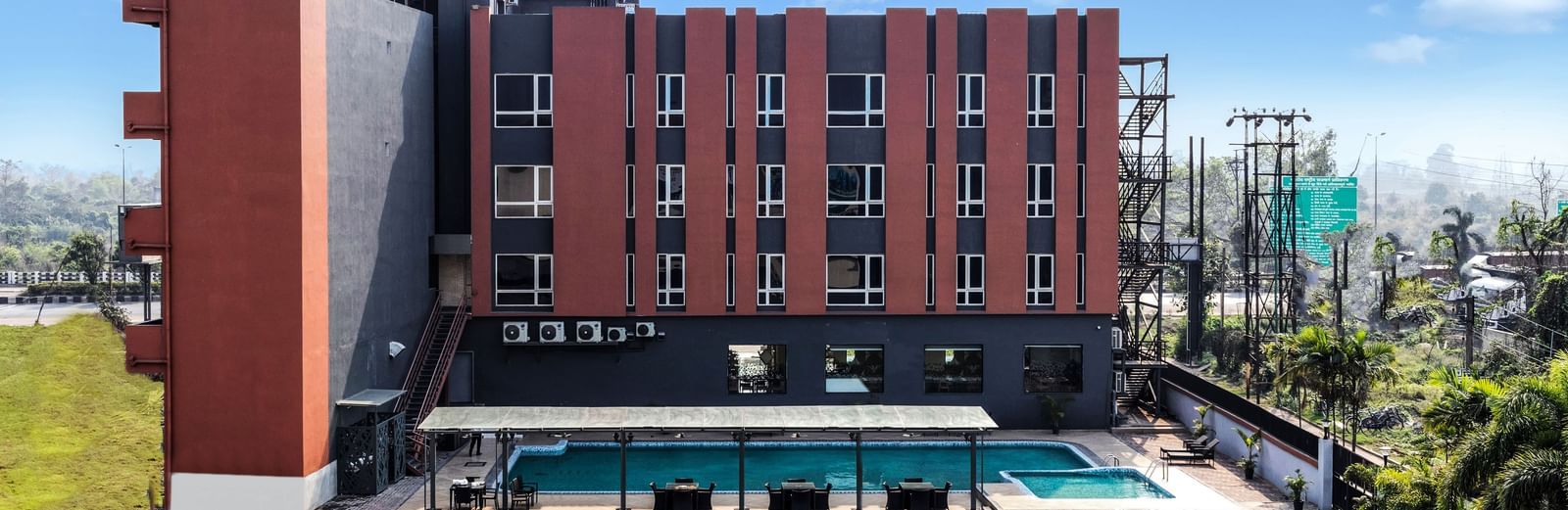 A modern hotel building with a swimming pool and green lawn under a partly cloudy sky | The Citi Residenci Hotel Banskopa