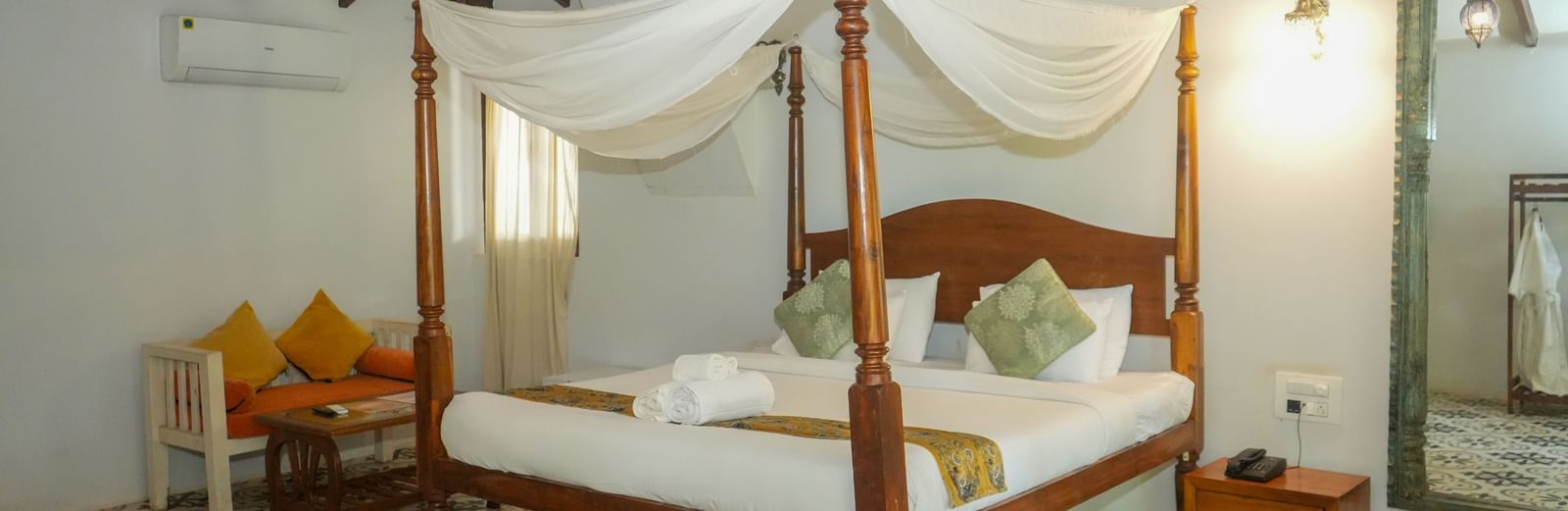 Bright room featuring a wooden four-poster bed with yellow cushions and detailed tiled flooring at De Soul Santé, Morjim.