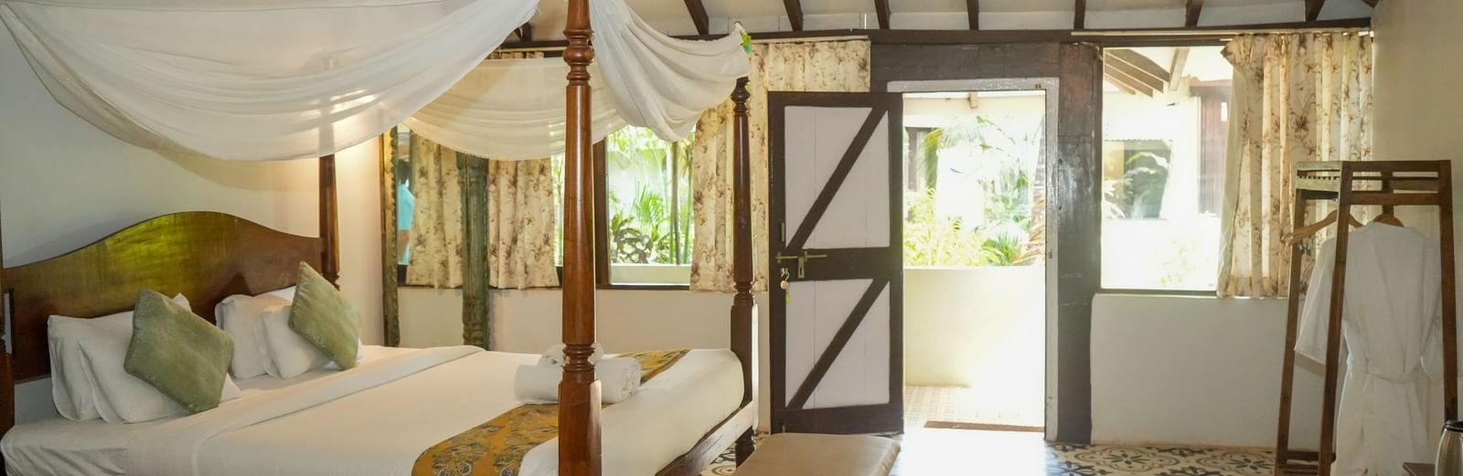 Side view of a spacious room with a large bed, wooden interiors, and a doorway leading outside at De Soul Santé, Morjim.