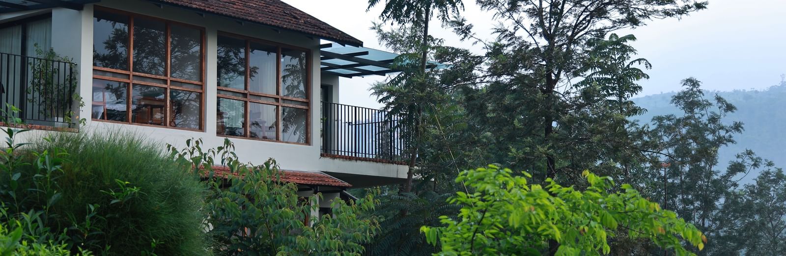  A building at Vaastha Vagamon, nestled amidst abundant foliage, with large windows overlooking a verdant landscape.