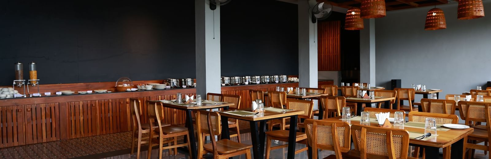  A well-appointed dining area at Vaastha Vagamon, featuring numerous tables and chairs, a buffet spread, and modern lighting fixtures.