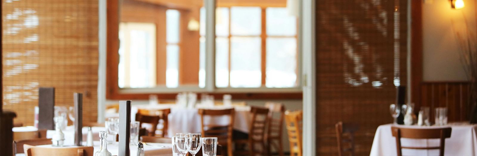 A dining room with wooden tables set with white tablecloths and chairs.