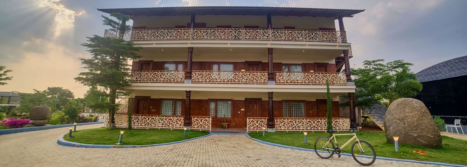 The exterior of a multi-storey building with a modern design and traditional elements, set on a paved area with green landscaping under a bright sky - Vintage Trails by Ilara