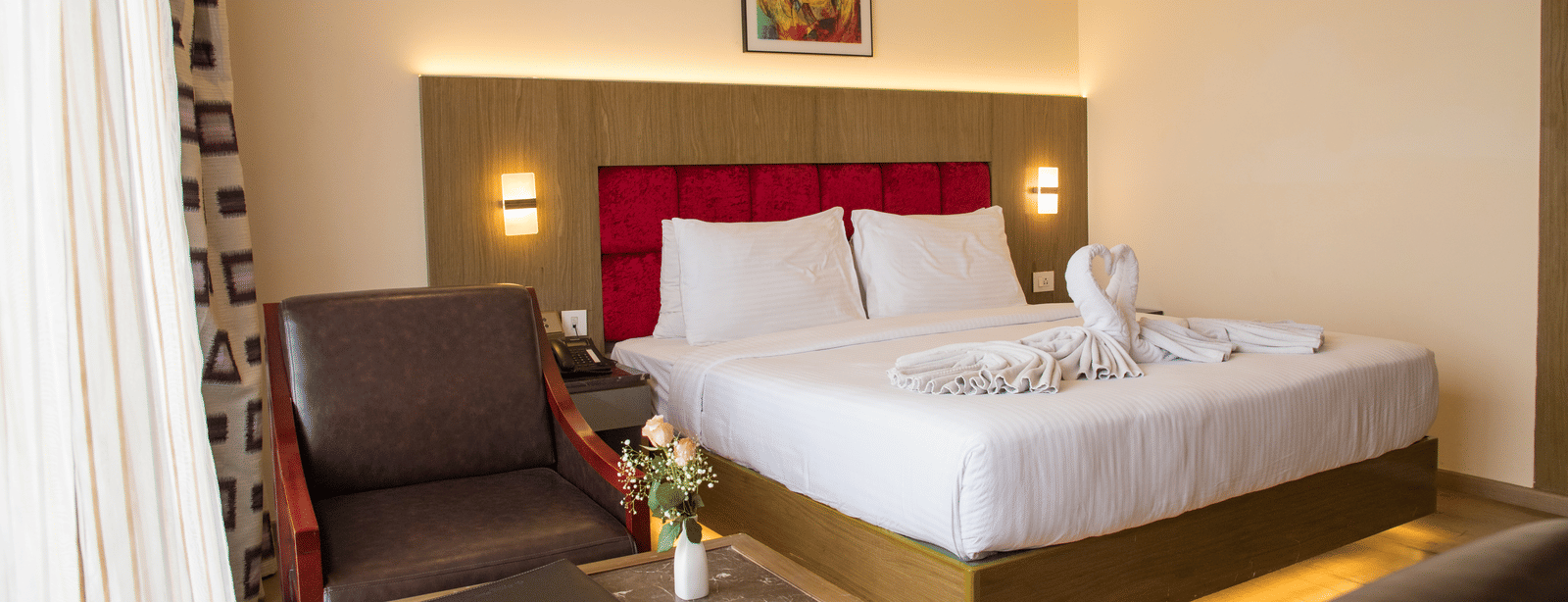 Side angle view of a double bed in a brightly lit Deluxe Room with a back lit headboard at the Benzz Park, Vellore.