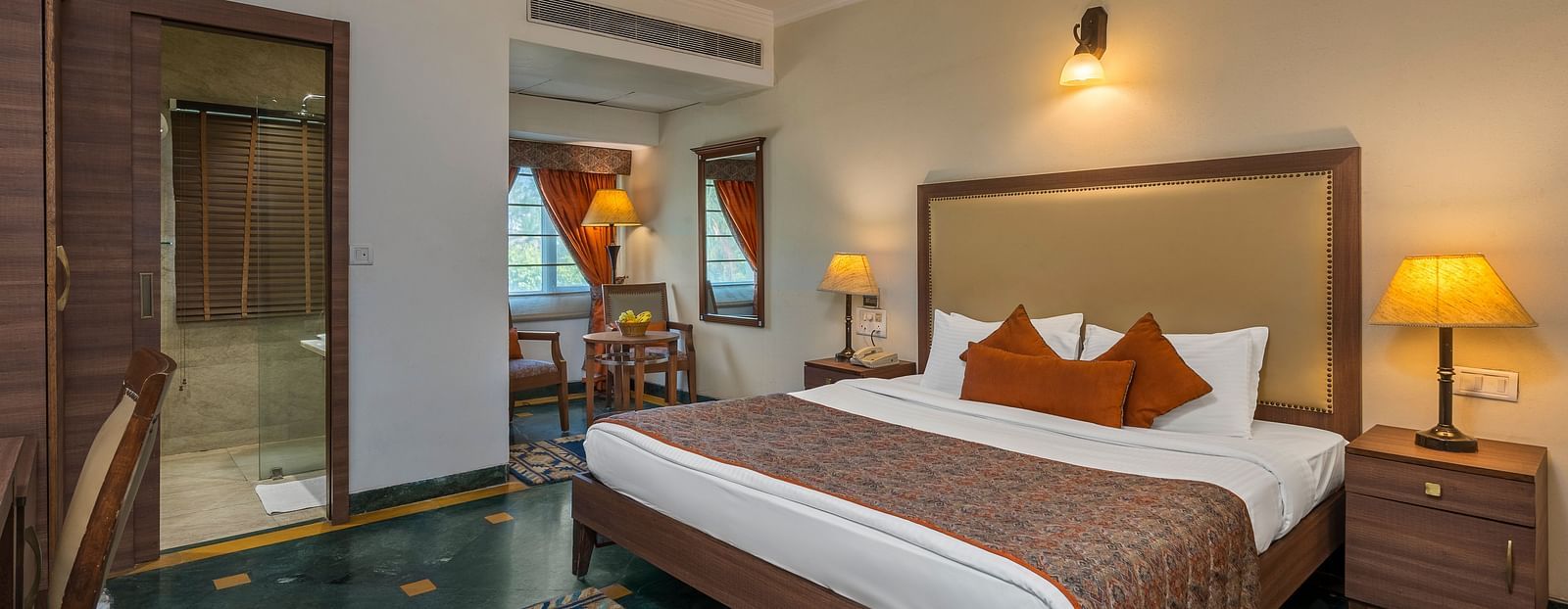 A bedroom with a large bed with side drawers placed on both sides of the bed, with an overhead lamp and side lamps - The Manor, Kashipur