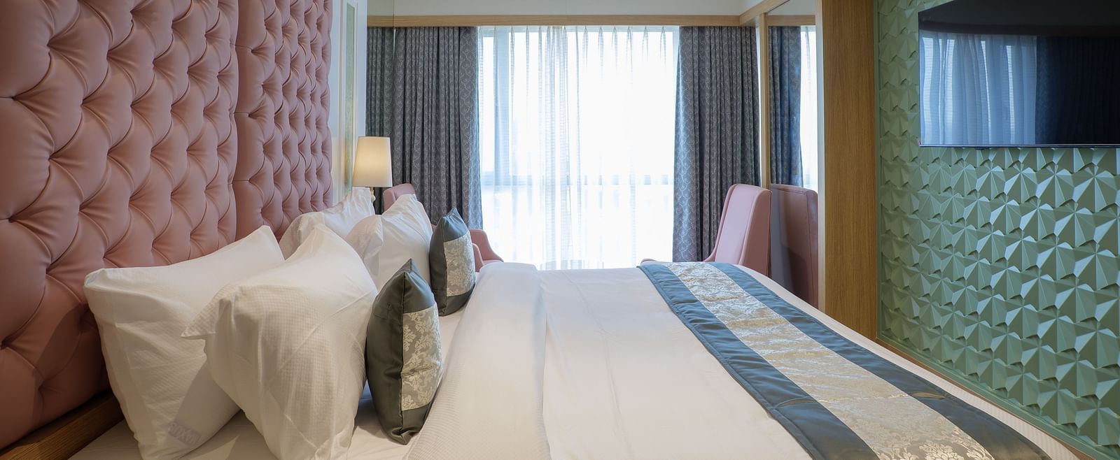 A modern hotel room features a bed with white linens and a television mounted on the wall - Melior Inn