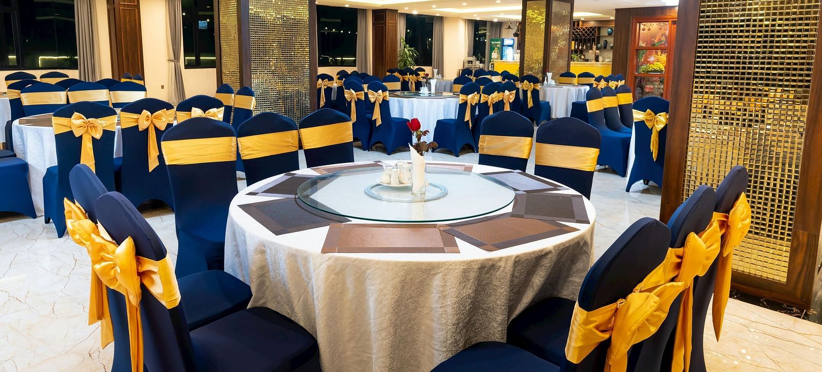 Elegant event space featuring round tables with floral arrangements, blue and gold decorated chairs, and decorative columns