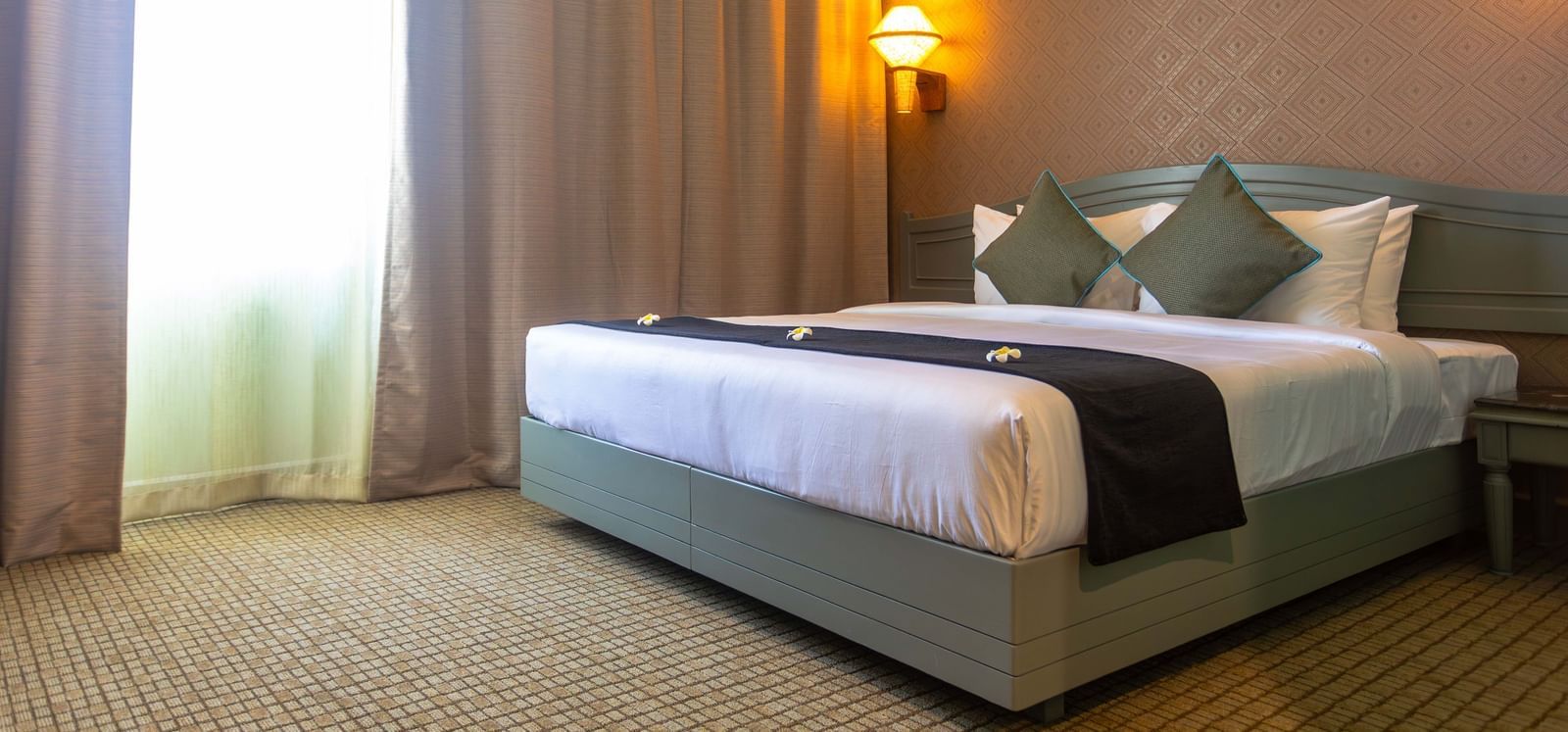 A guest room at Shilton International, Kochi, featuring a large bed, and a window with natural light.