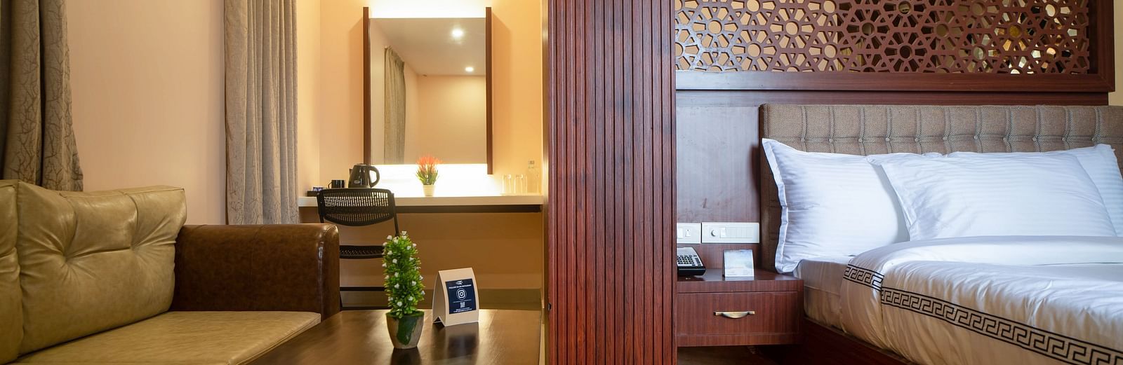 A hotel room interior featuring a sofa, coffee table, bed, and decorative wall panel | Mansha Hotels