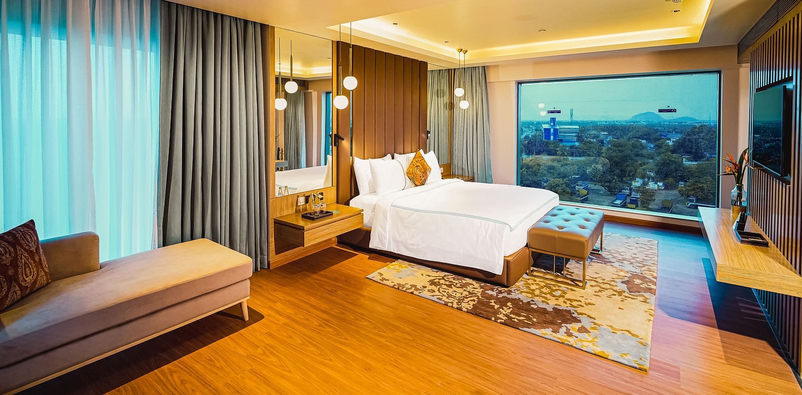 A beautiful image of a hotel room in Madurai with a large bed, a couch, and a wall-mounted television