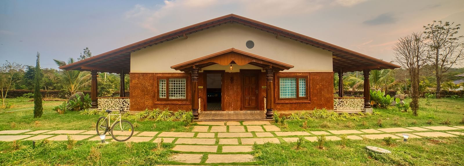The front exterior of a single-storey building with a sloping roof and a prominent entrance, accessed by a path of large stepping stones through a green lawn. - Vintage Trails by Ilara
