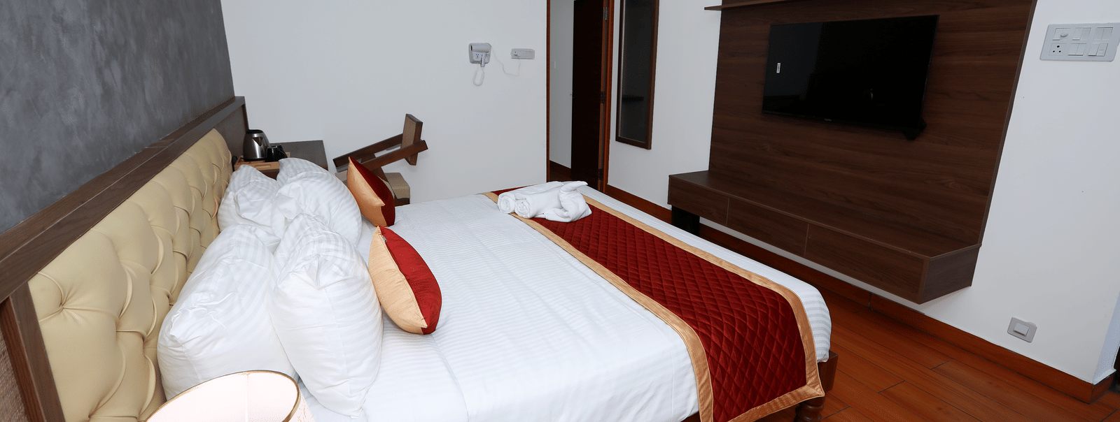 Side view of the double bed kept in the Standard Room of WOW Naturefull Resorts, Yercaud, with a dark grey-coloured wall behind the tufted headboard.
