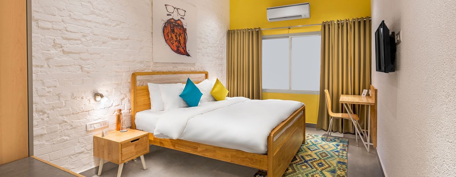 An interior image of the standard room at Bedzzz Varanasi showcases a spacious layout, featuring a comfortable double bed, a cozy floor mat, a stylish study table and chair, a charming coffee table, elegant curtains, an air conditioner for a refreshing amb