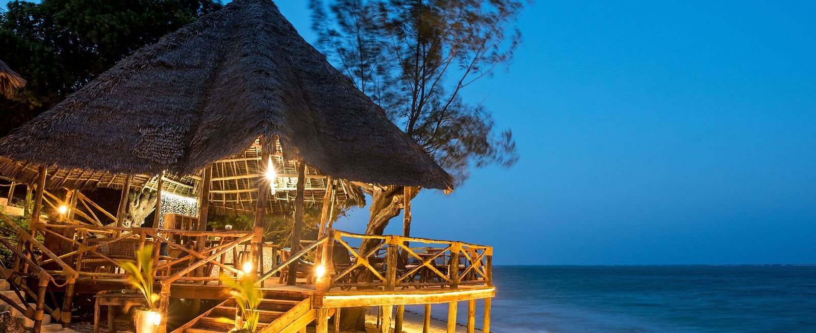 A beautifully lit beachside bar with a thatched roof, set against the backdrop of the ocean at twilight at Shooting Star Boutique Hotel