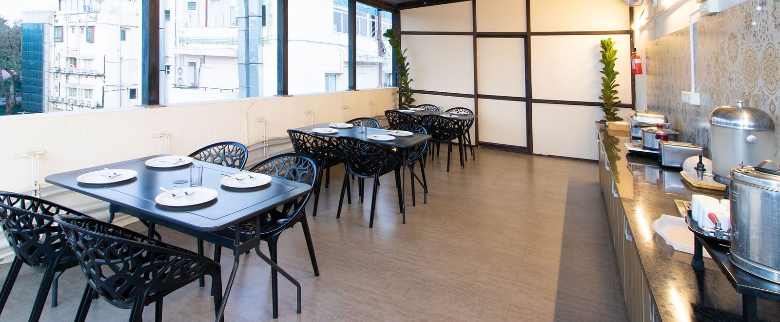 A covered outdoor dining area with tables and chairs, offering a view of the surrounding urban landscape at Sanctum Suites Indiranagar, Bangalore.