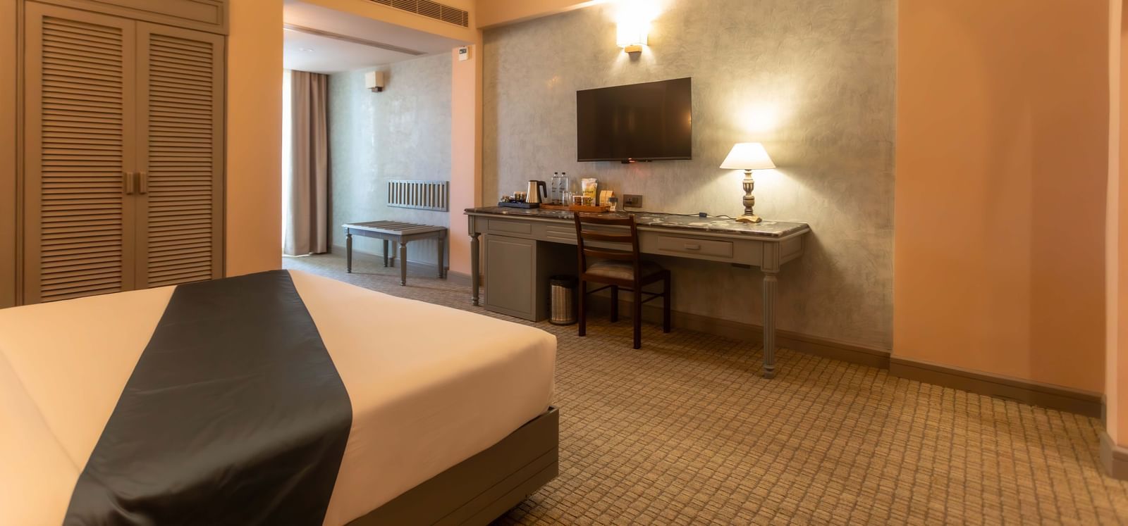 A guest room at Shilton International, Kochi, with a bed, a desk, and a television.