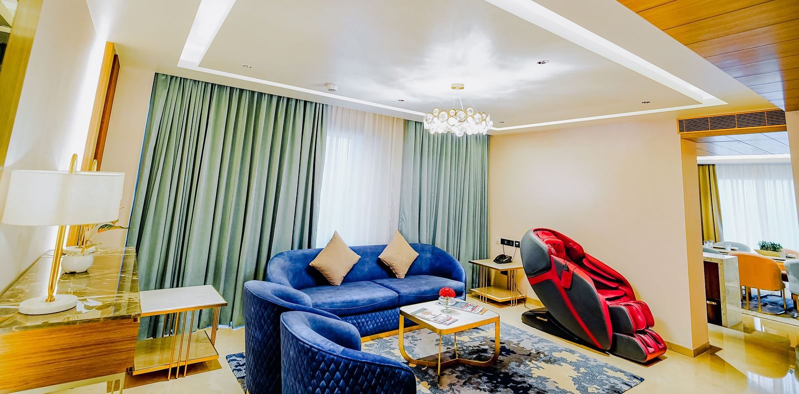 A low angle shot of the living area in Grand Velammal Suite with sofa and blue chairs placed around a coffee table and a massage chair on the side