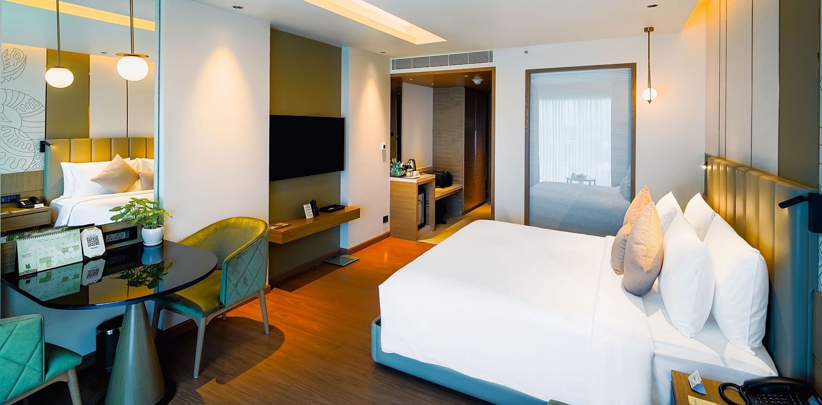 An image of a room with a large bed, work desk, and a wall-mounted television