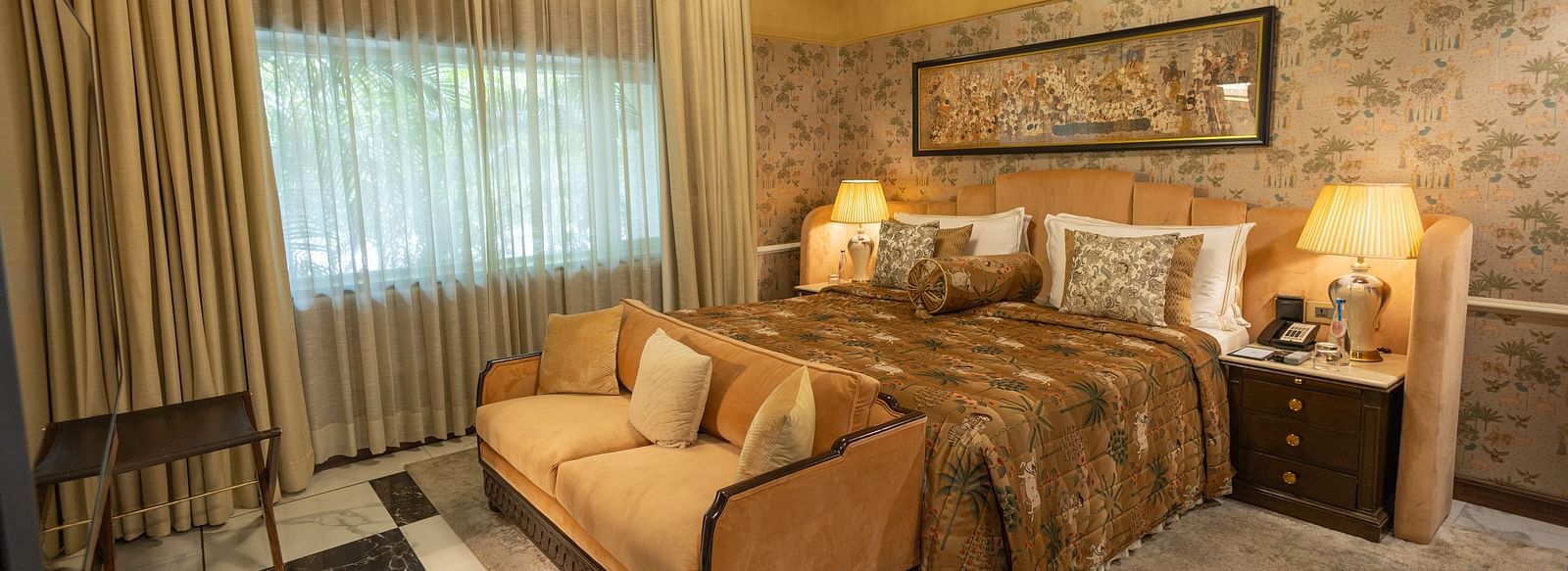 Executive Suite at The Claridges New Delhi, featuring a cosy king sized bed, a sofa placed in front, and a bedside lamp