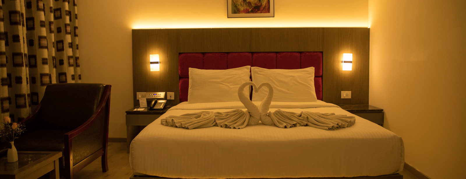 A cosy Deluxe Room with warm lighting featuring a double bed alongside an armchair at the Benzz Park, Vellore.