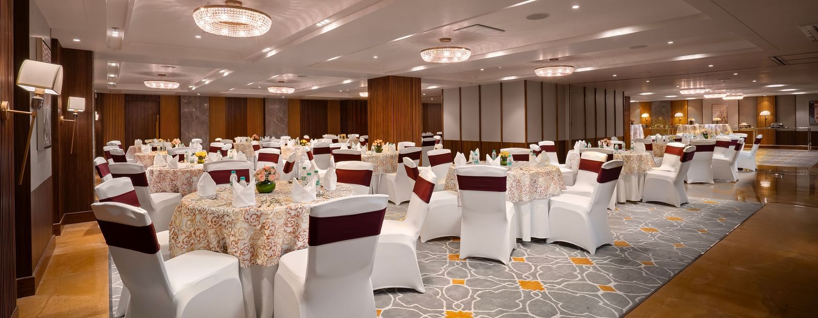 A spacious conference hall with round tables covered in tablecloths and chairs. and the room is decorated with chandeliers and wall lamps.