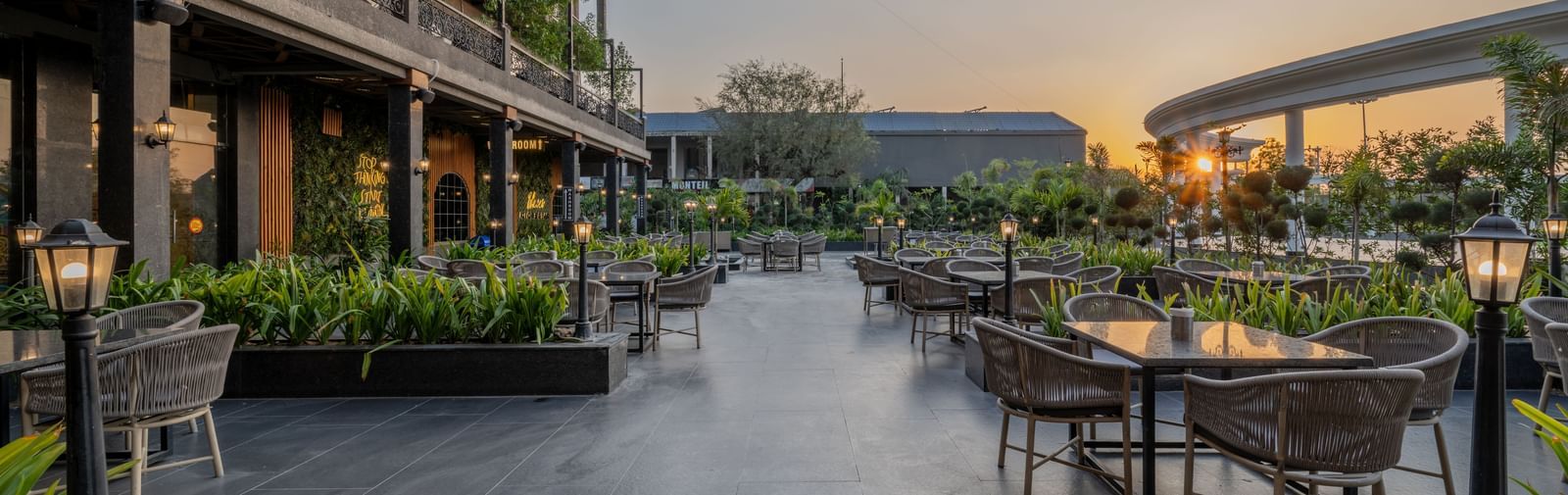 Outdoor seating area at Hotel Highway King, Bagru, with tables, chairs, greenery, and the hotel building in the background.