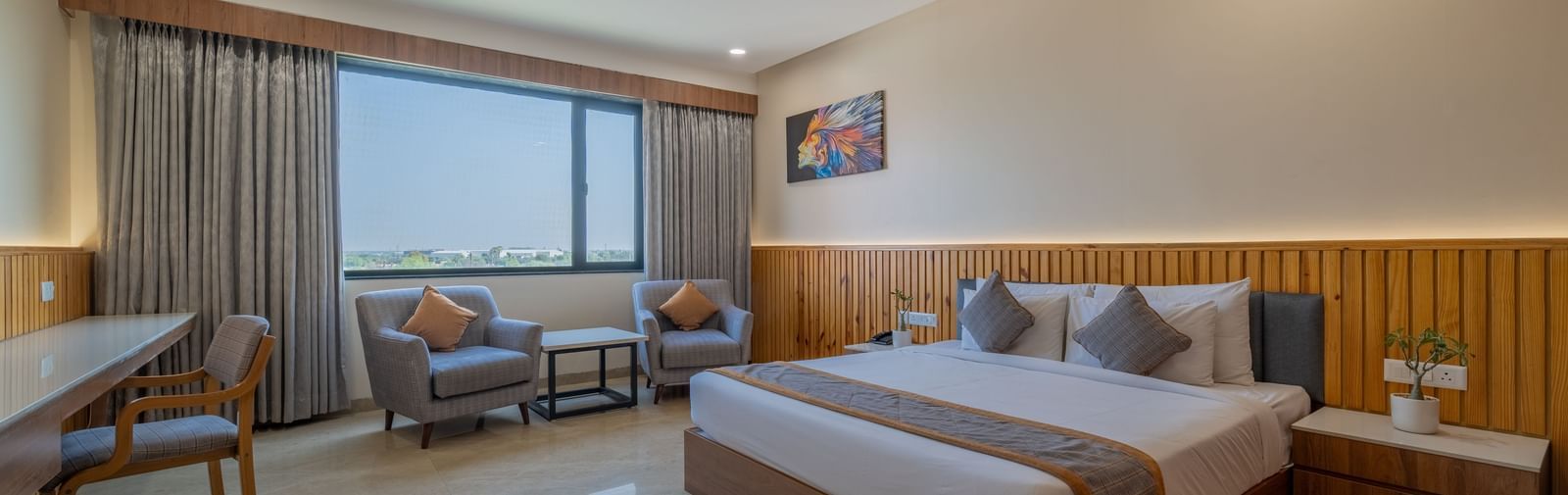 A bedroom at Hotel Highway King, Bagru, featuring bedside tables, desk, seating area, ceiling fan, and large window.