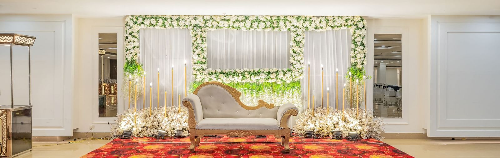 Indoor wedding stage setup with floral arrangements and red carpet at Hotel Highway King, Bilaspur.