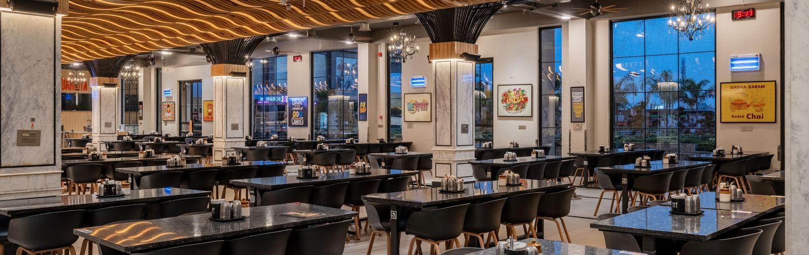 The spacious dining area at Hotel Highway King, Kishangarh, features modern tables and chairs under a wavy ceiling design.