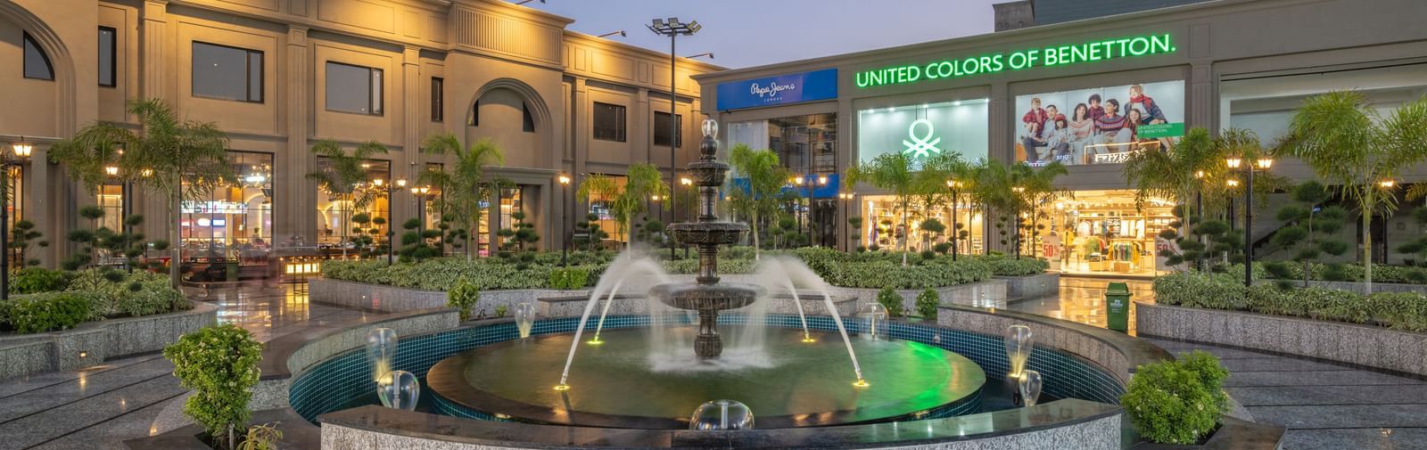 Evening view of fountain and courtyard at Hotel Highway King, Kishangarh with signage and building in the background.