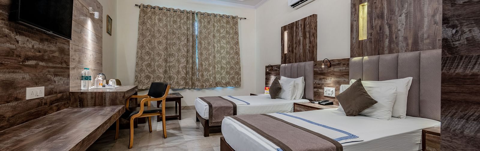 A spacious guest room with multiple beds and a TV at Hotel Highway King Shahpura.
