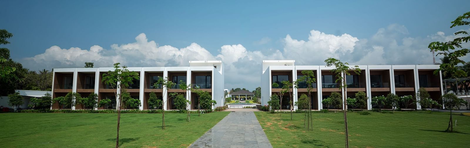  A lush green lawn at The Shore Trishvam, Pondicherry divided by a pathway in the middle with a clear blue sky in the background.