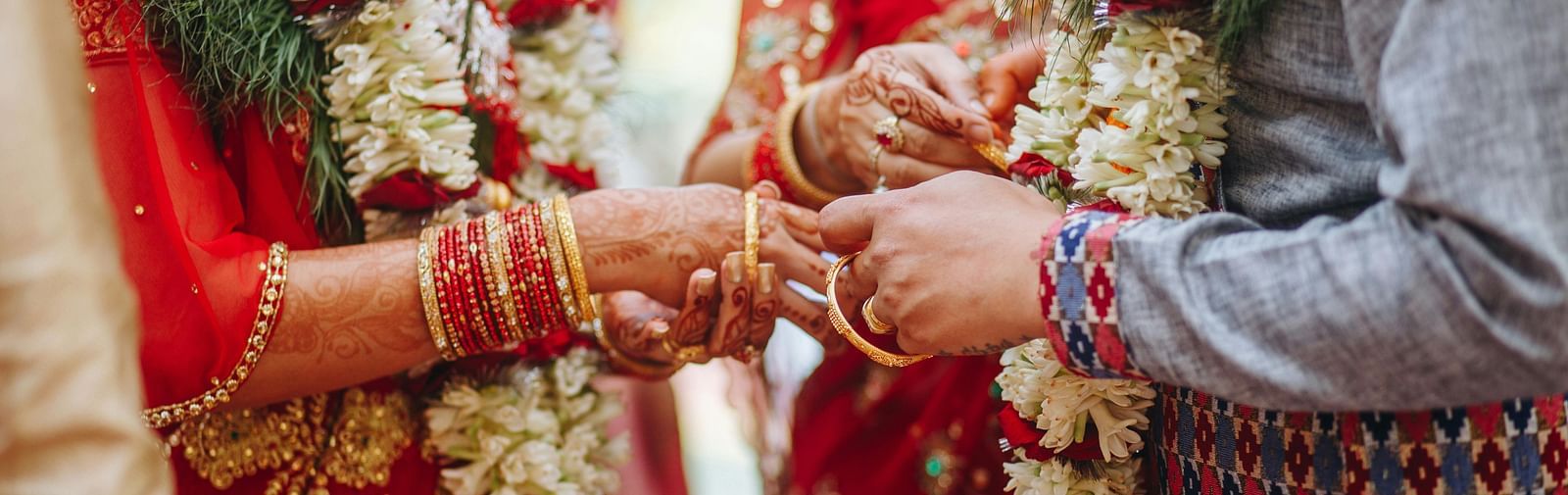 a couple wearing flower garlands exchanging rings with people around them
