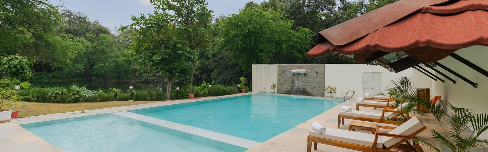 a beautiful image of the swimming pool at aranya vilas nestled amidst lush greenery featuring sun loungers at the pool side