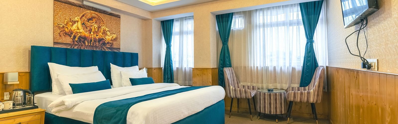 Deluxe Room Avianna Seven Seas, Deluxe Room with a king size bed, inviting ambiance, wooden bedside table, and a large window with curtains drawn along with a wall mounted television at Avianna Seven Seas, Darjeeling.