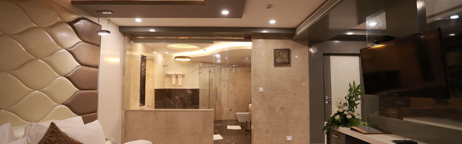 side view of a bedroom with a large bed facing the television and entrance to the washroom on the other side - Hotel Park Elanza, Chennai