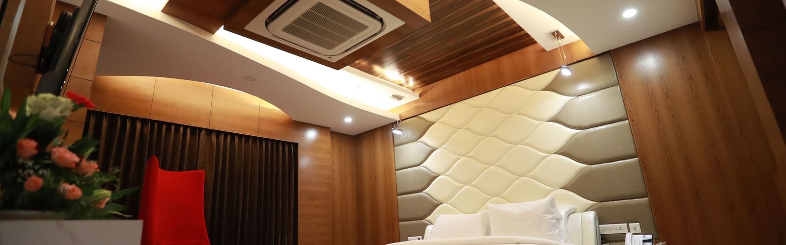 a bedroom with a large bed and a red chair with false ceiling and overhead lighting - Hotel Park Elanza, Chennai