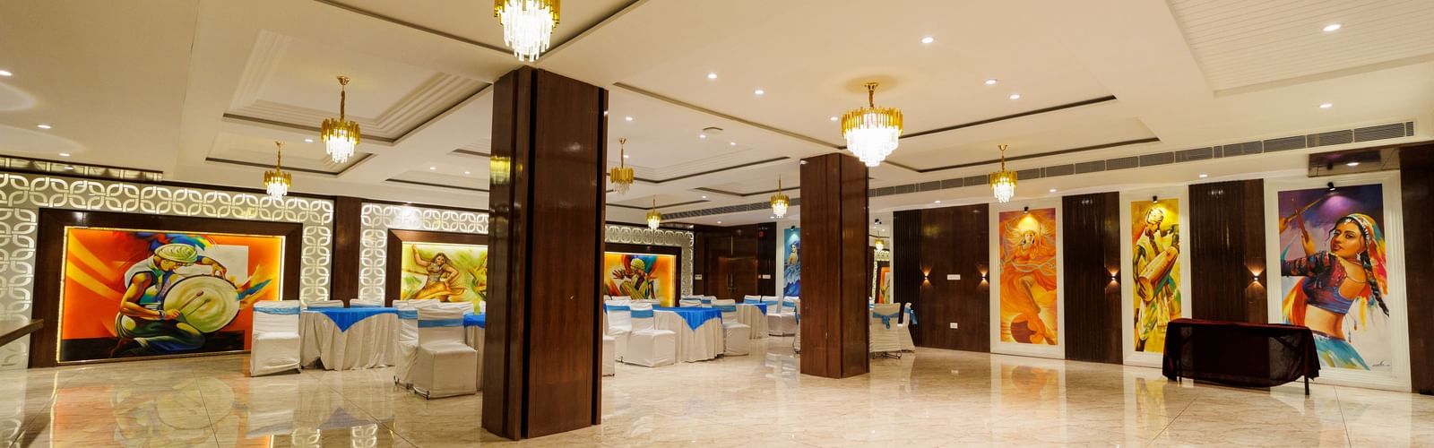 Banquet hall at Inde Reva Resorts Rishhikesh with marble flooring, ceiling lights, and artwork displayed along the walls.