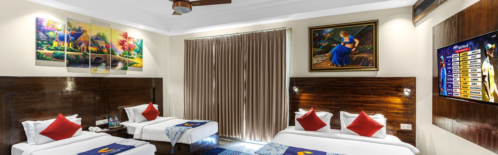 Well furnished huge room with a king size bed and twin beds featuring a ceiling fan, artwork above bedside table, and TV unit opposite the beds at Inder Reva Resorts Rishhikesh.